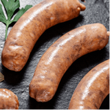 Three uncooked sausages on a black slate with a piece of green garnish